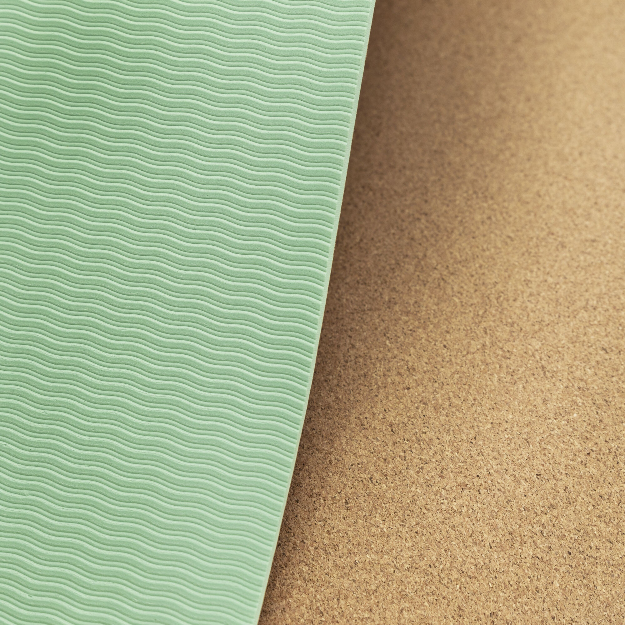 Zbliżenie na miętową matę do jogi o teksturowanej powierzchni, obok korkowej płyty.