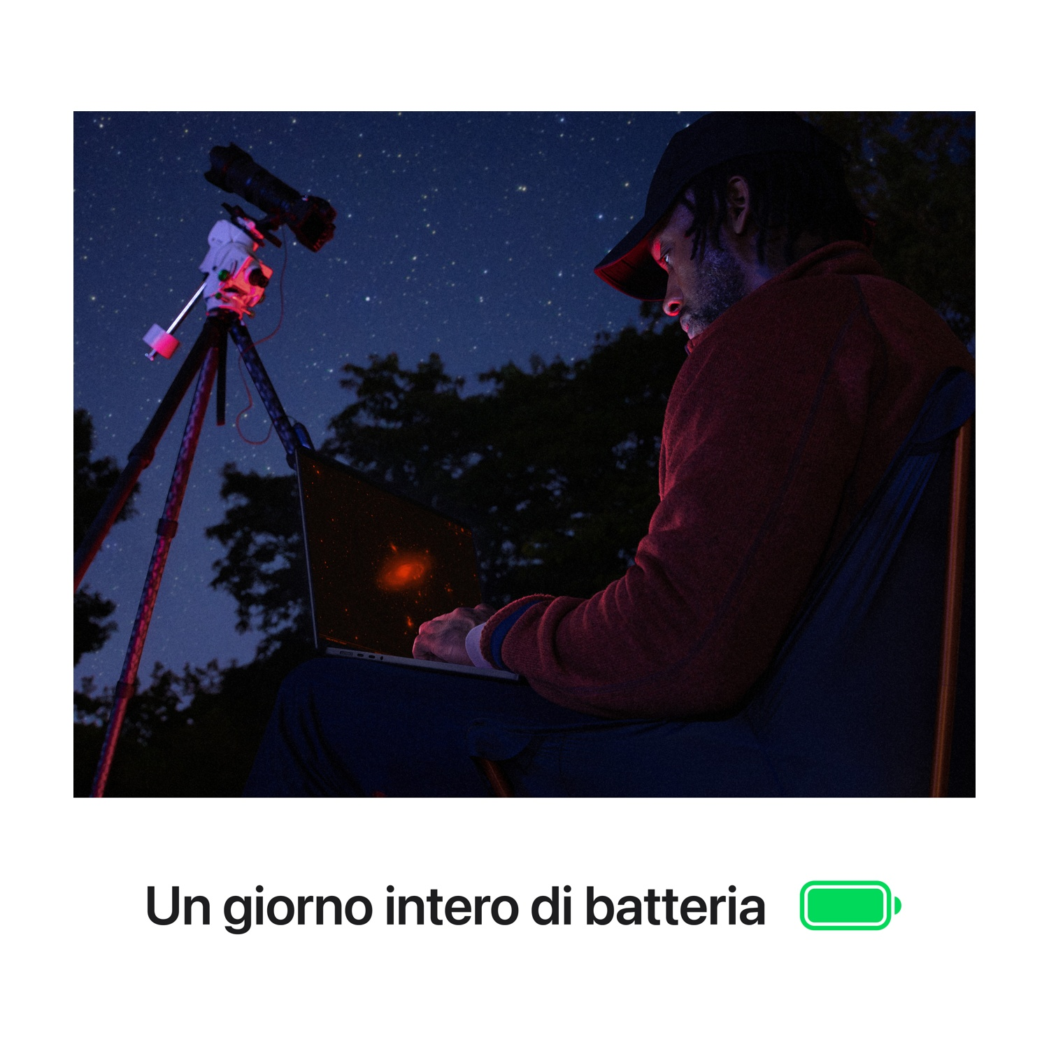 Uomo che usa il laptop di notte. Telescopio installato vicino. Testo: Un giorno intero di batteria.