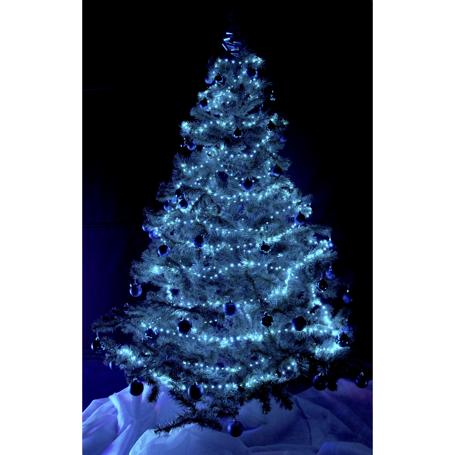Albero di Natale illuminato di blu con ornamenti e luci, su sfondo blu scuro.