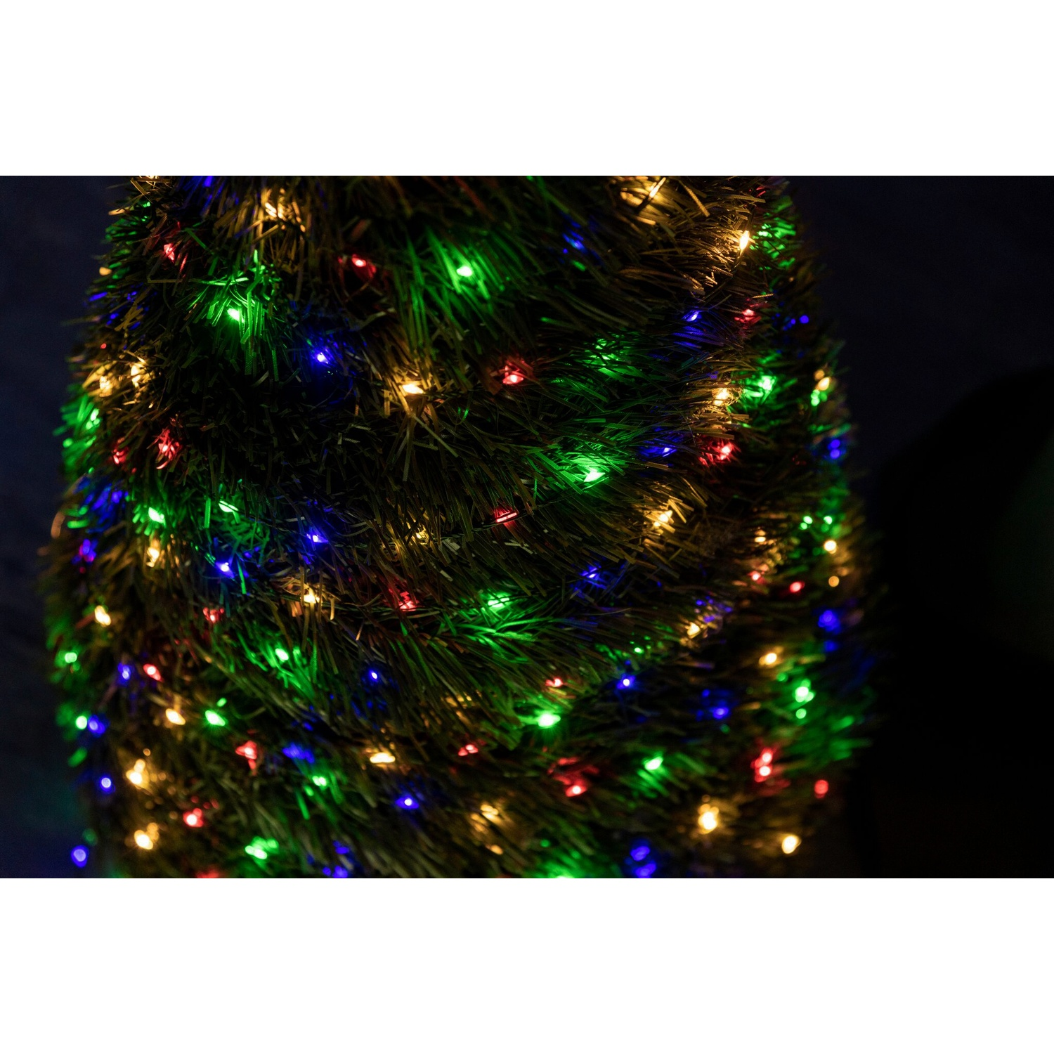Un albero di Natale con luci a LED colorate è illuminato su sfondo scuro.