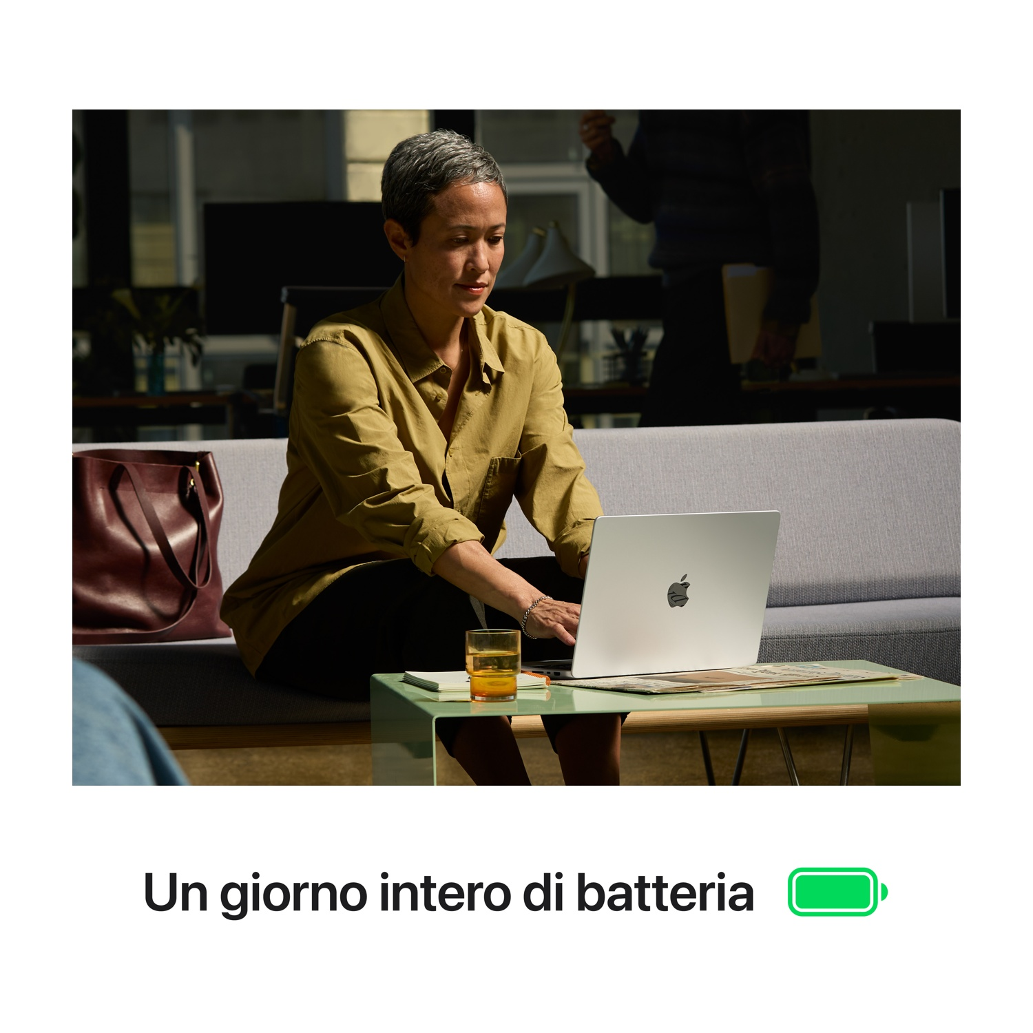 Donna usa laptop con bevanda. Sfondo: divano e persona.
