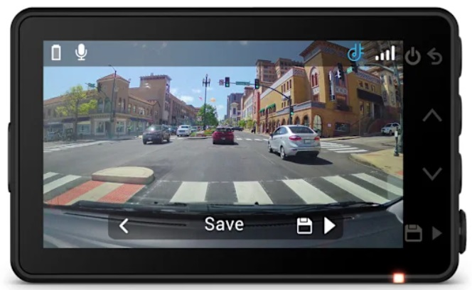 Ekran kamery samochodowej z drogą z samochodami, budynkami i przejściami dla pieszych. Kamera jest czarna.