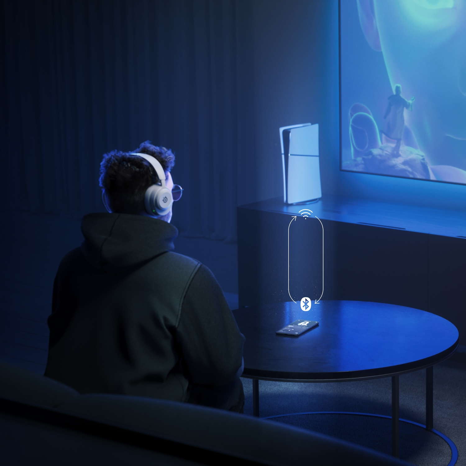 Une personne regarde la TV avec un téléphone. Une console est près de la TV.