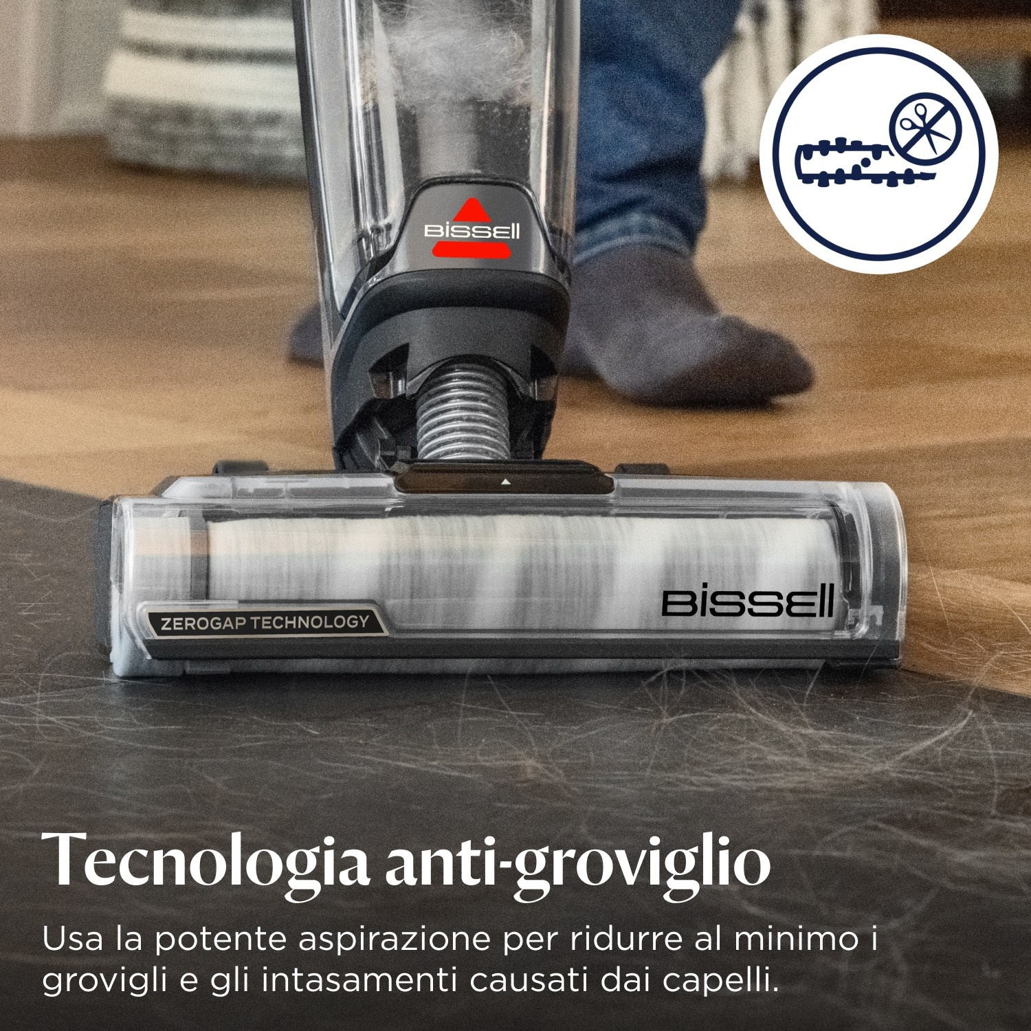 Viene mostrata una testina per aspirapolvere. Il testo dice 'Tecnologia ZeroGap' e 'Tecnologia anti-groviglio'. Pavimento in legno e grigio.