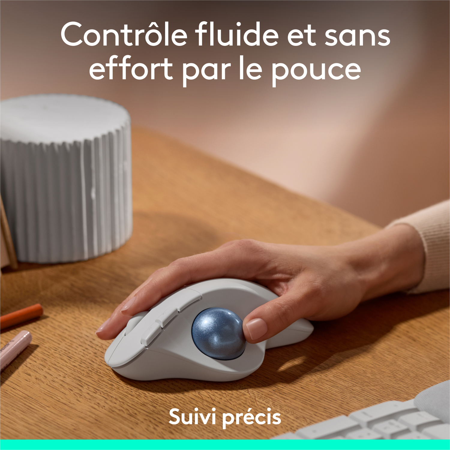 Une main utilisant une souris trackball grise avec une boule bleue, avec du texte en français.
