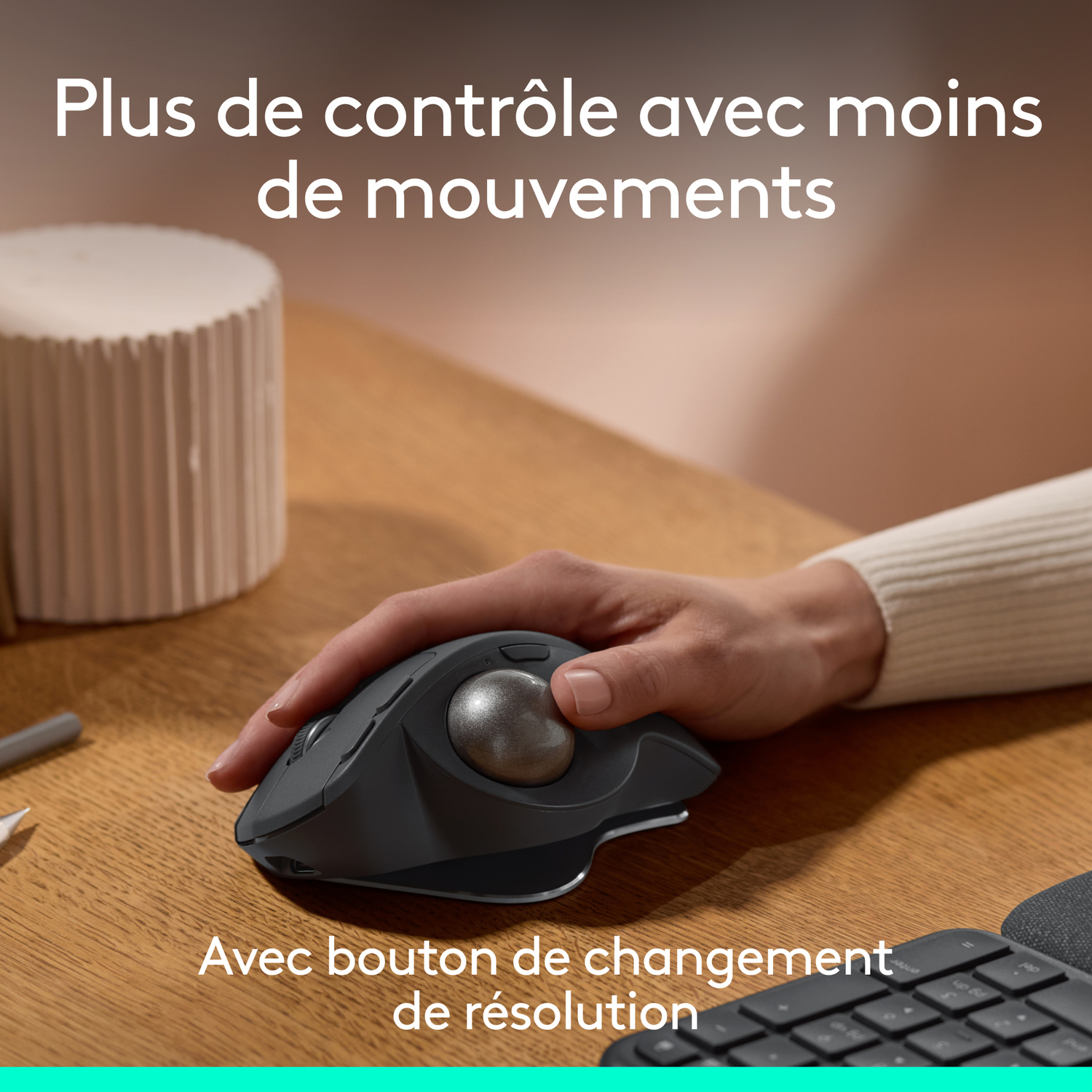 Une main utilisant une souris trackball noire sur un bureau.