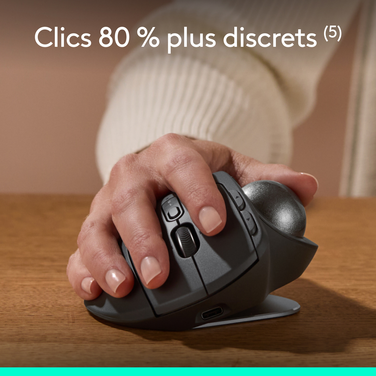 Main tenant une souris grise. La souris est sur une table en bois.