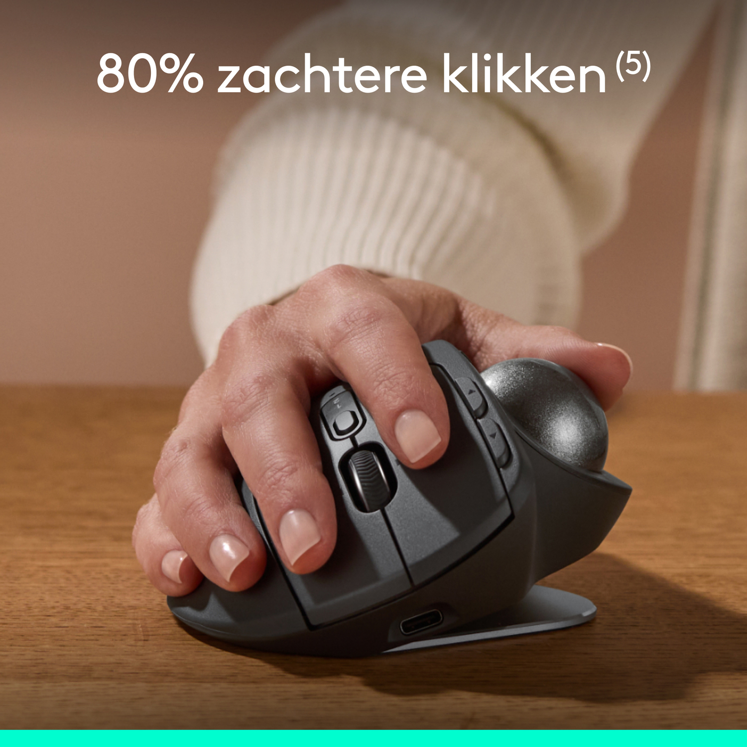 Hand using a dark grey trackball mouse. The device sits on a light grey base.