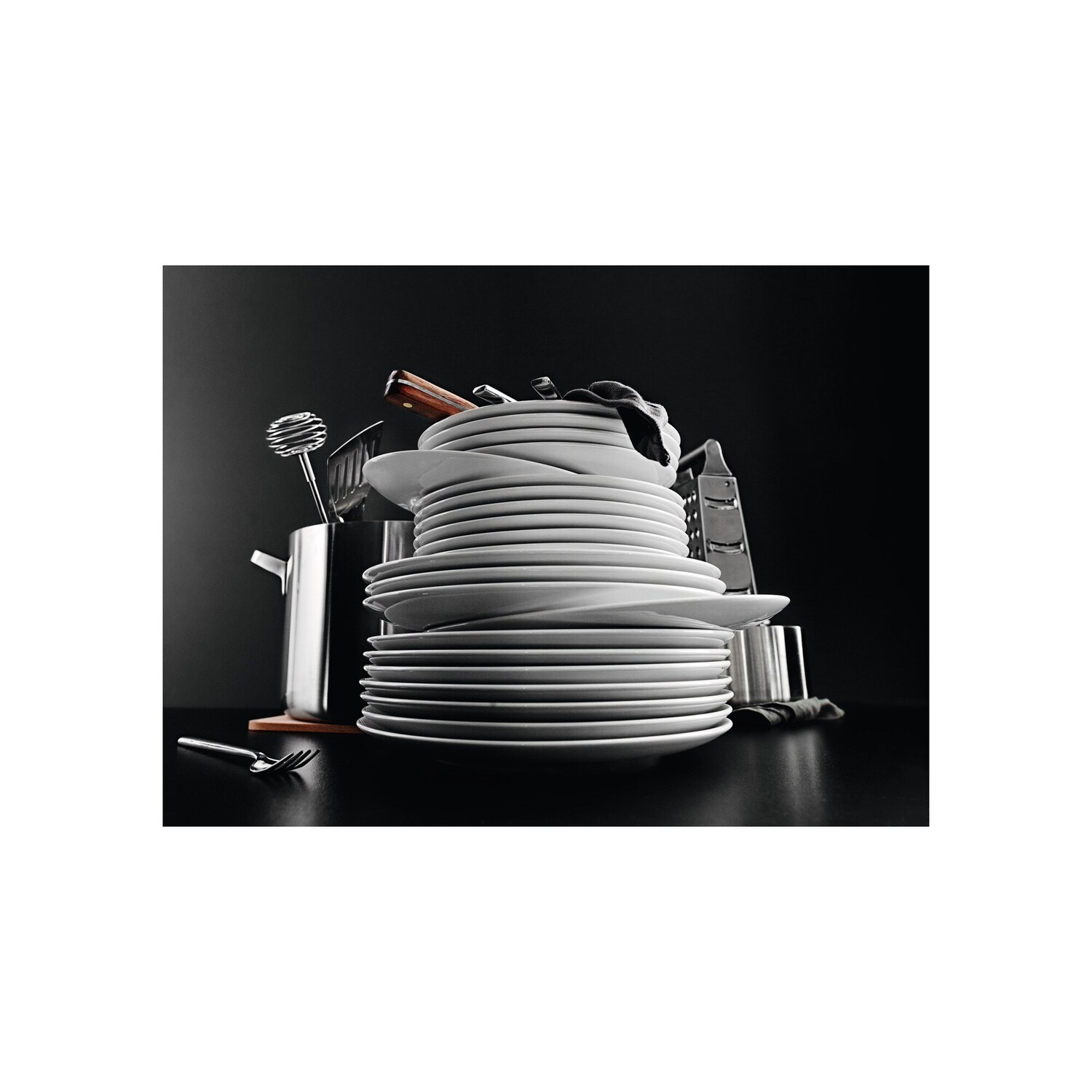 A stack of white plates, utensils, and other kitchen tools on a black surface.