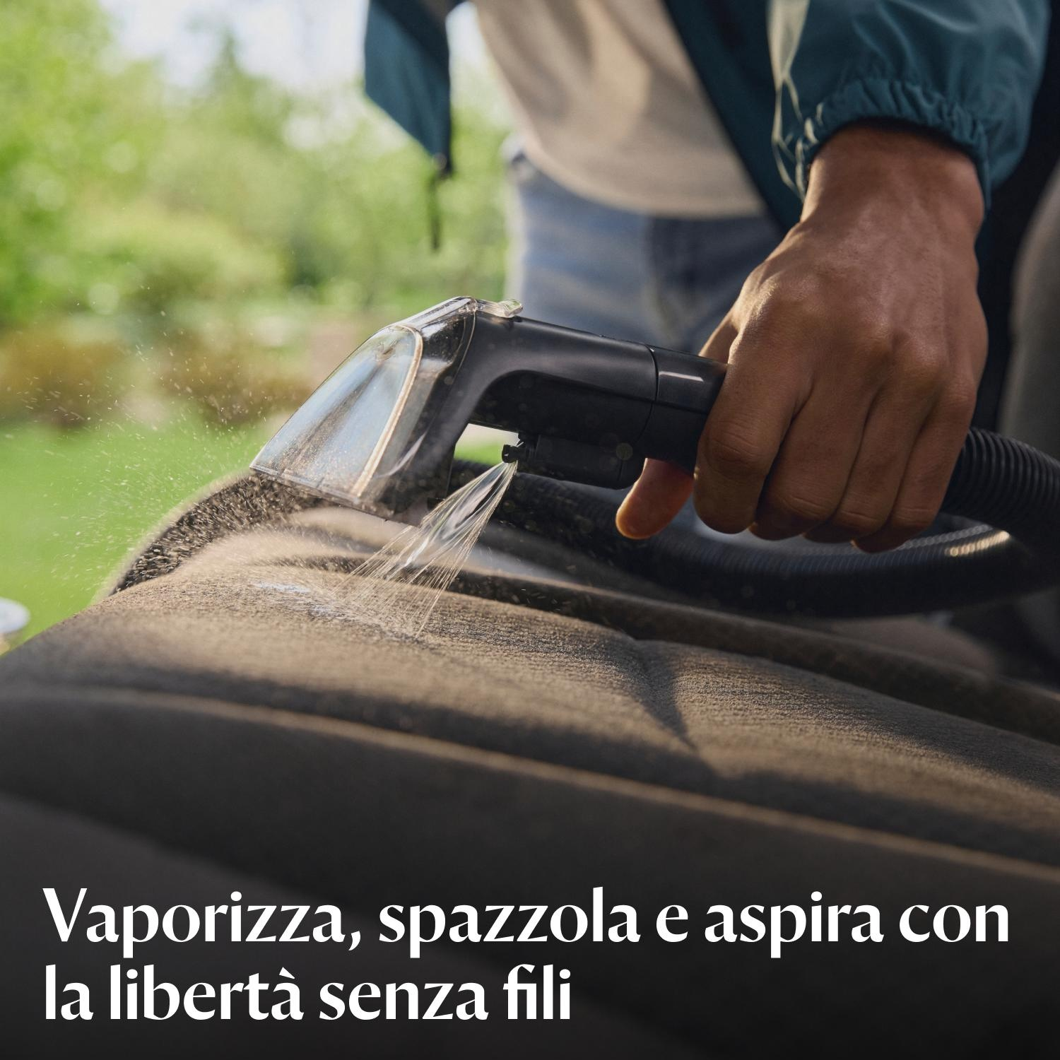 Una persona sta passando l'aspirapolvere su un sedile dell'auto con un aspirapolvere portatile. L'acqua viene spruzzata sul sedile.