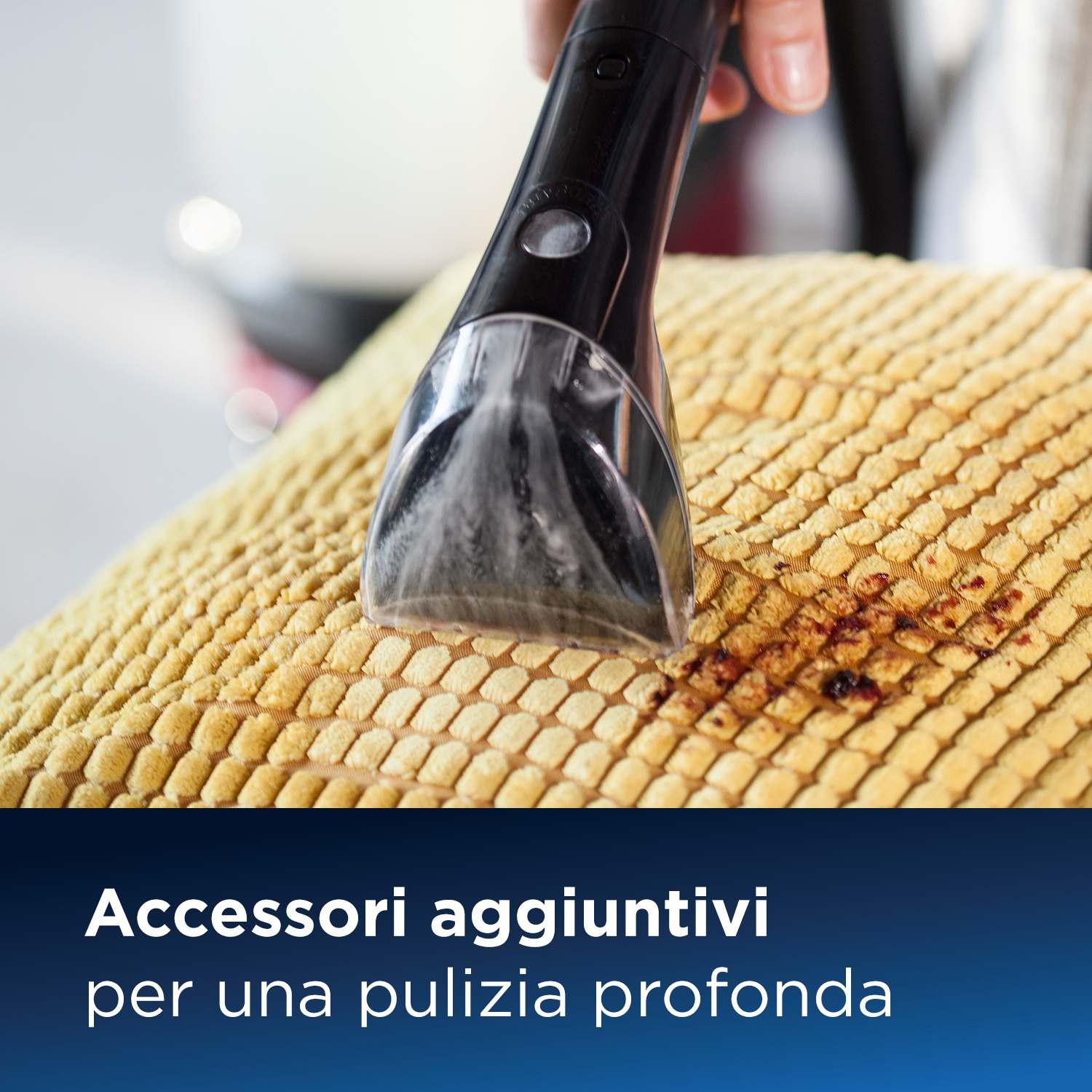 Una mano usa uno strumento di pulizia su un cuscino giallo. Macchie marroni sul cuscino.