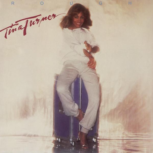 Album borító: Tina Turner. Fehér ruhát visel, kék ládán ül.