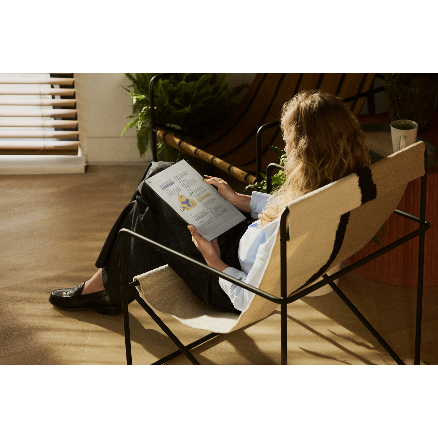 Vrouw zittend in een stoel, leest een document. Ze zit in een comfortabele stoel in een goed verlichte kamer.