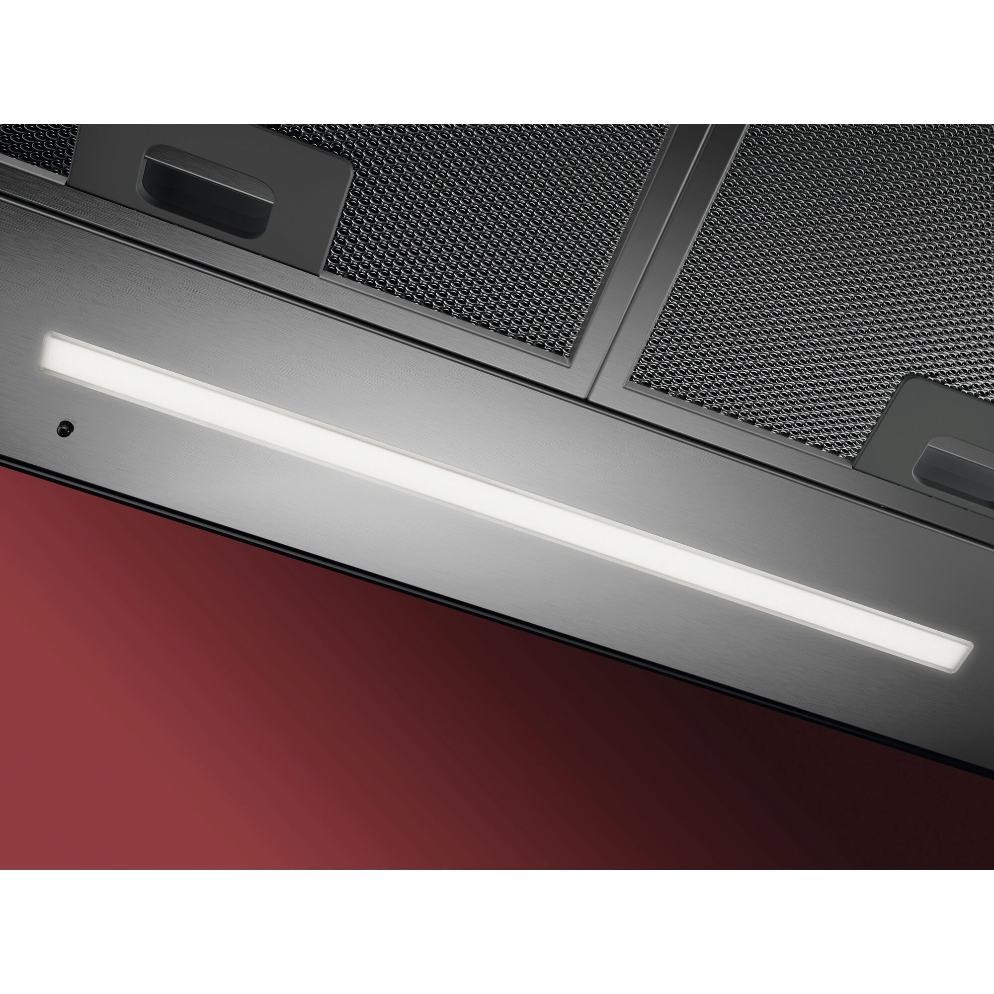Nahaufnahme einer modernen Küchenhaube mit hellem LED-Lichtstreifen und rotem Hintergrund.