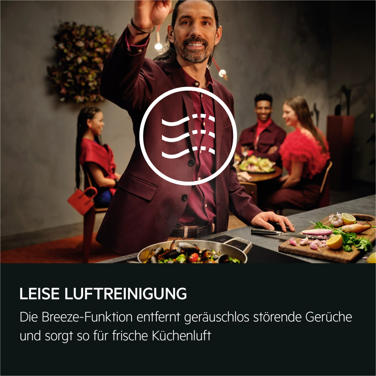Mann in bordeauxrotem Anzug hält Utensil. Leute am Tisch mit Essen. Text: Leise Luftreinigung.