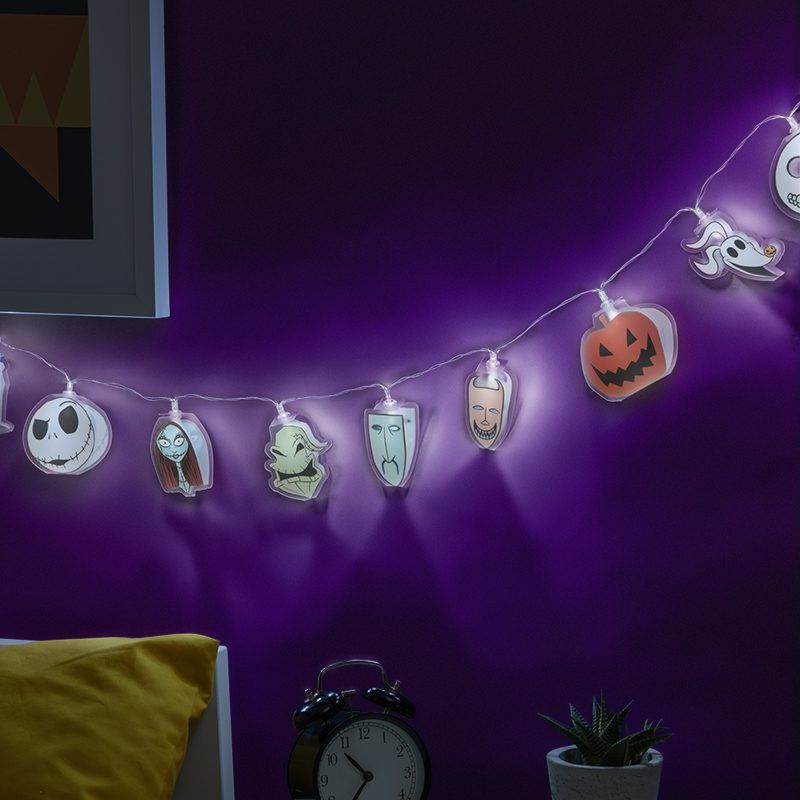 Halloween lámpák karakter kivágásokkal lila falon, ébresztőórával és növénnyel.