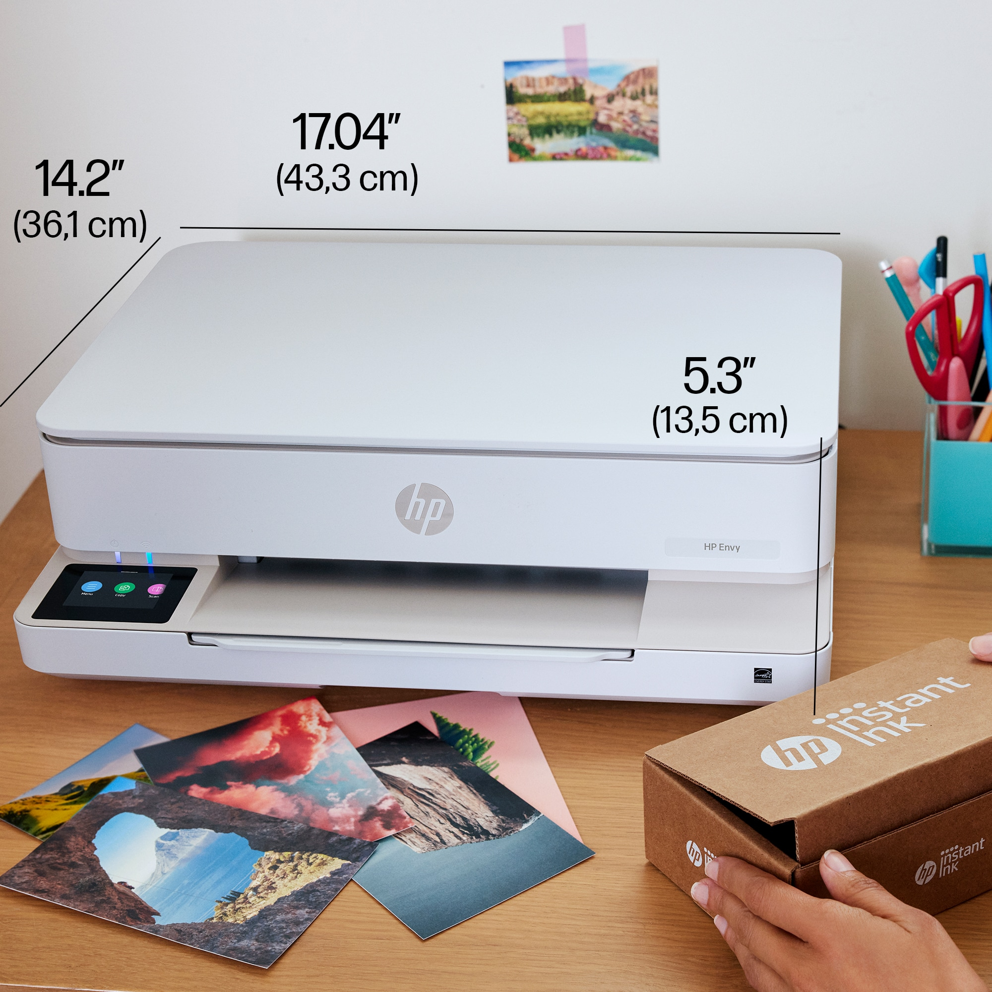Ein weißer Drucker mit Abmessungen, Fotos und einer Instant Ink-Box stehen auf einem Holztisch.