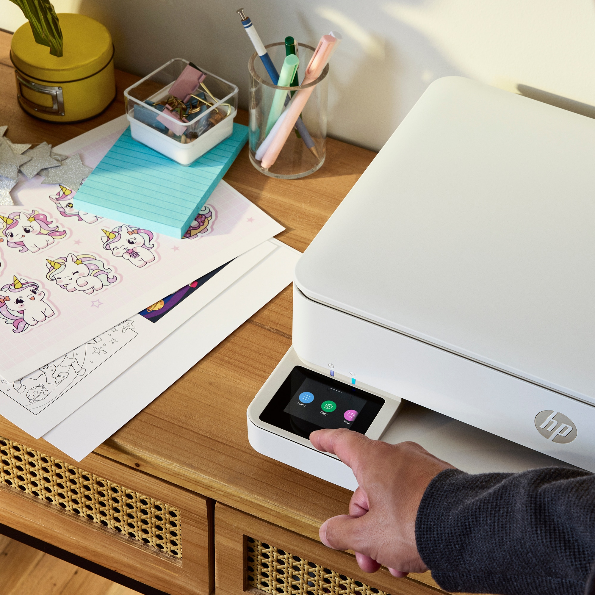 A person's hand is touching the screen of a white printer. Papers and office supplies are visible.