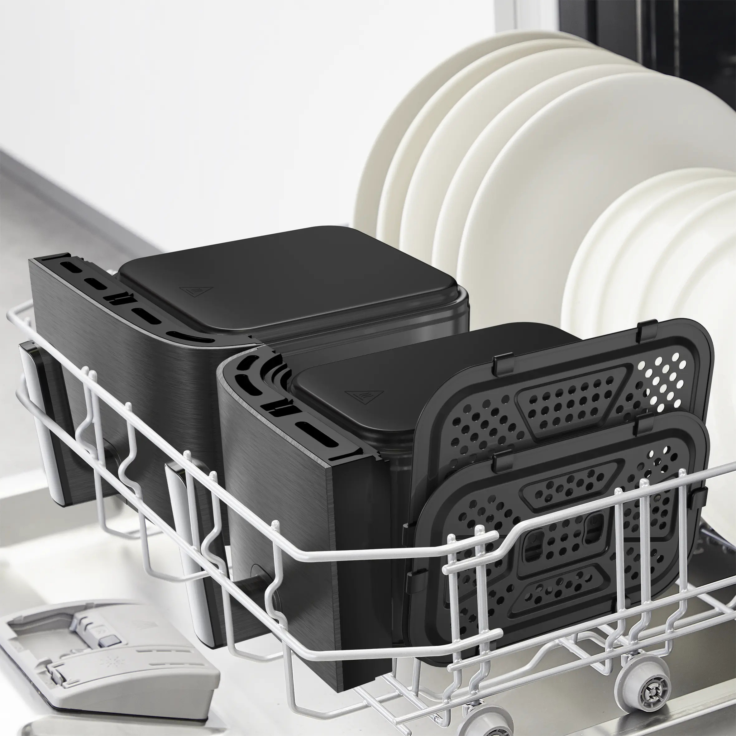 Czarne elementy frytownicy w koszu zmywarki, z białymi talerzami w tle.