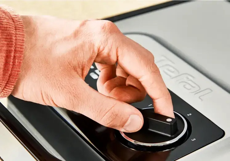 Dłoń obracająca pokrętło na czarno-szarym urządzeniu.