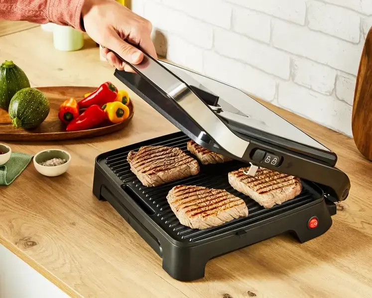 Osoba grilluje steki na czarnym grillu. Warzywa z boku.