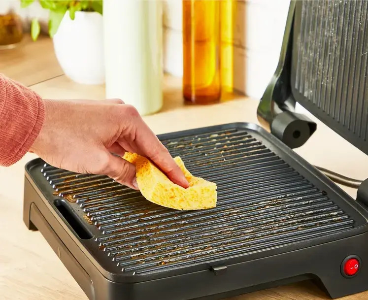 Osoba czyści grilla. Grill jest gorący i brudny. Osoba używa gąbki.