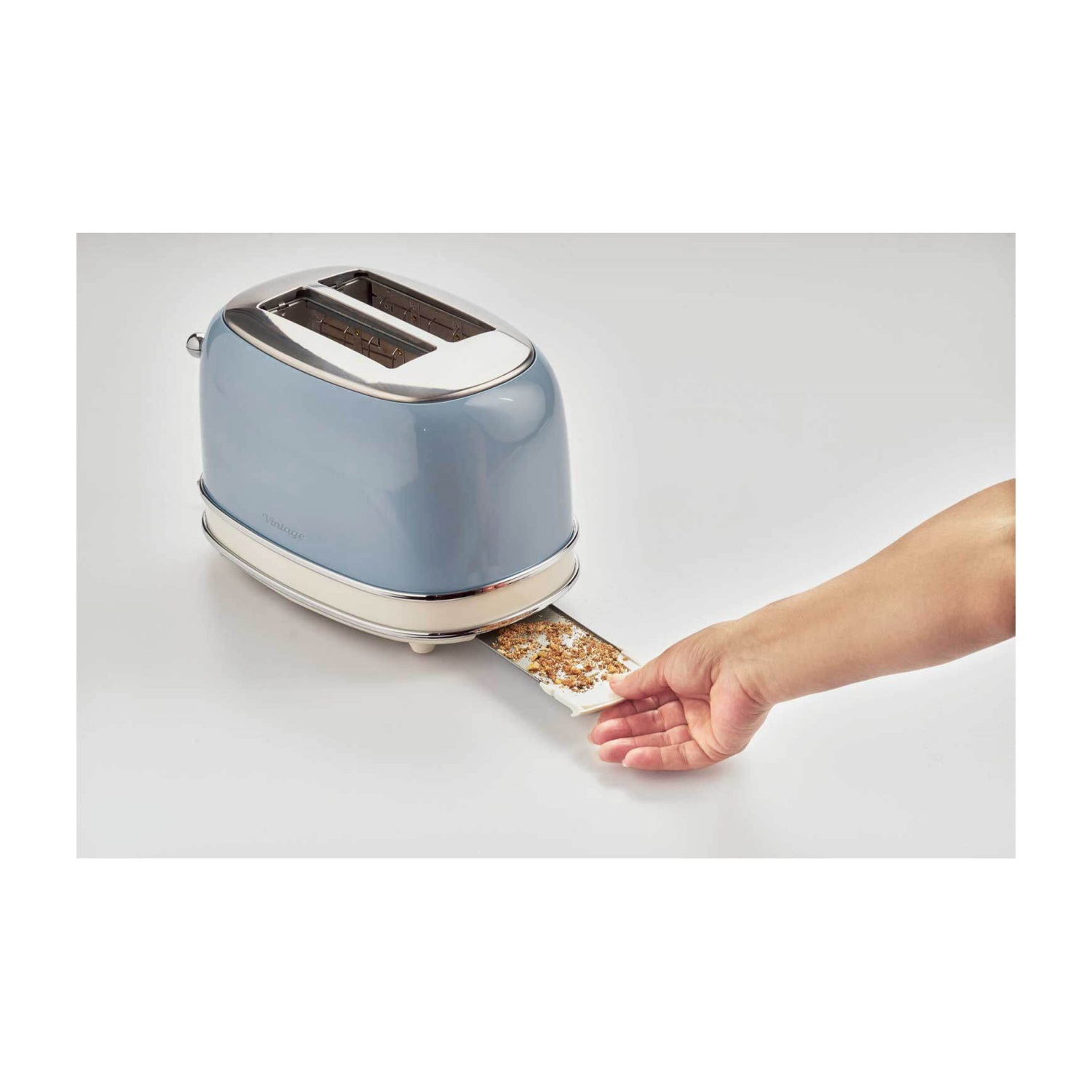 Una mano toglie il toast da un tostapane blu e argento in stile vintage su una superficie bianca.