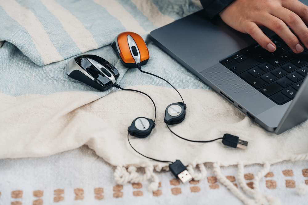 Dwie przewodowe myszy komputerowe i laptop na kocu. Ręka osoby na klawiaturze laptopa.
