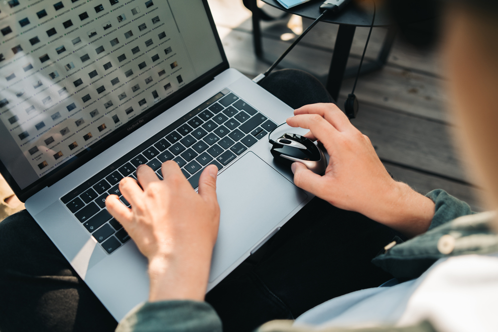 Osoba korzysta z laptopa, pisząc na klawiaturze i trzymając mysz, z rozmytym tłem.