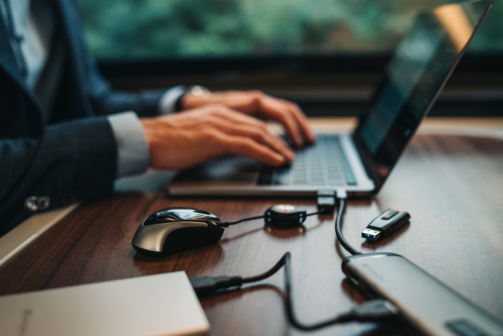 Osoba korzystająca z laptopa, podłączonego do myszy, pendrive'a i power banku.