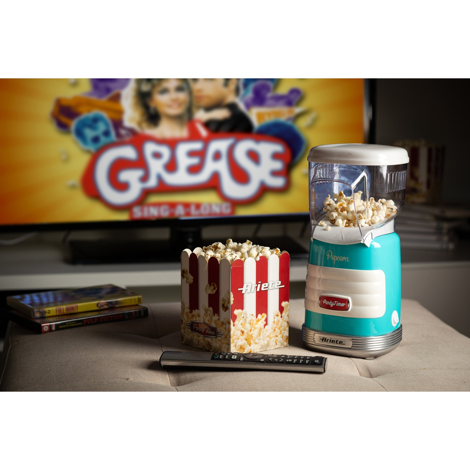 Macchina per popcorn e scatola di popcorn con poster del film Grease sullo sfondo. Telecomando sul tavolo.