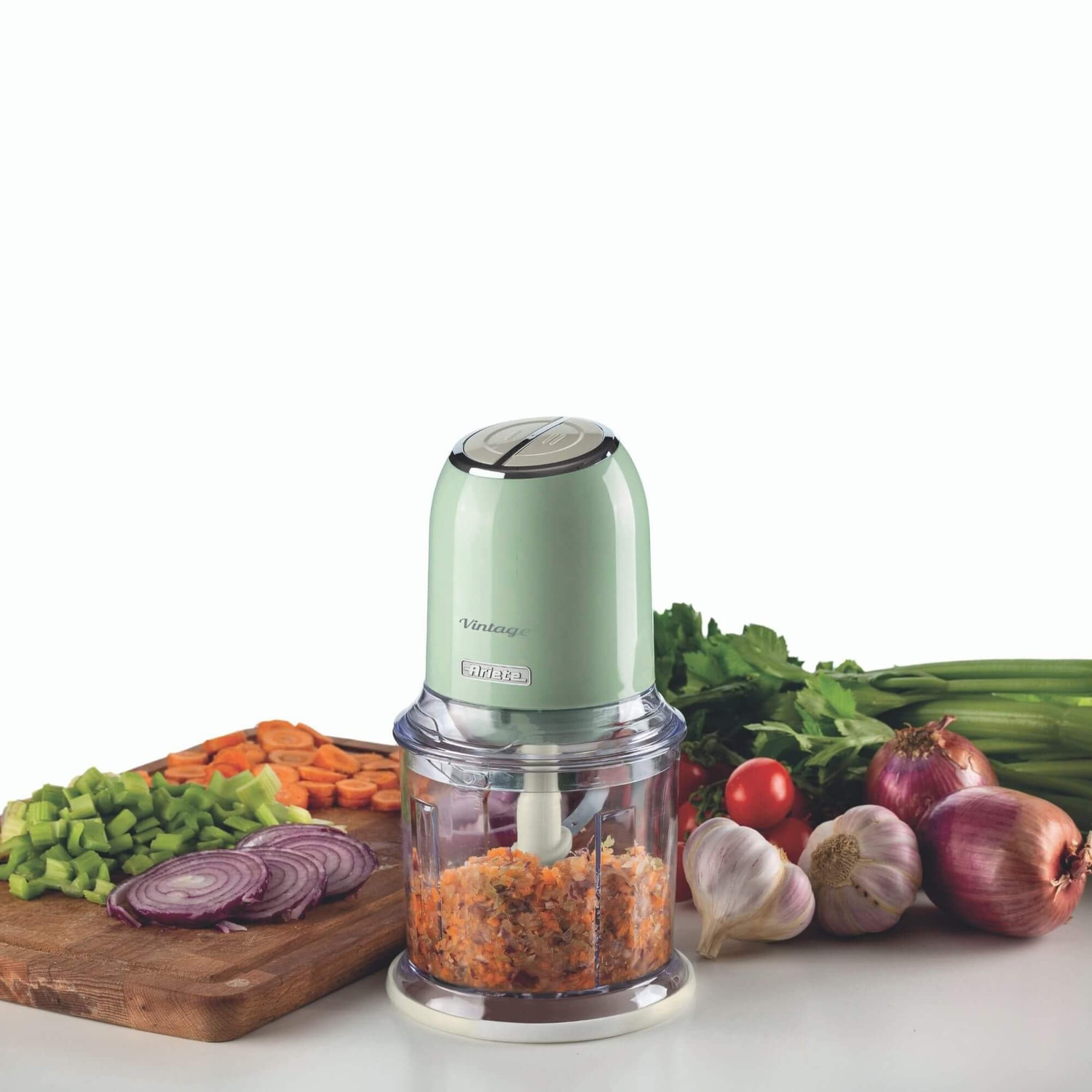 Un tritatutto verde con verdure ed erbe tritate su una superficie bianca.