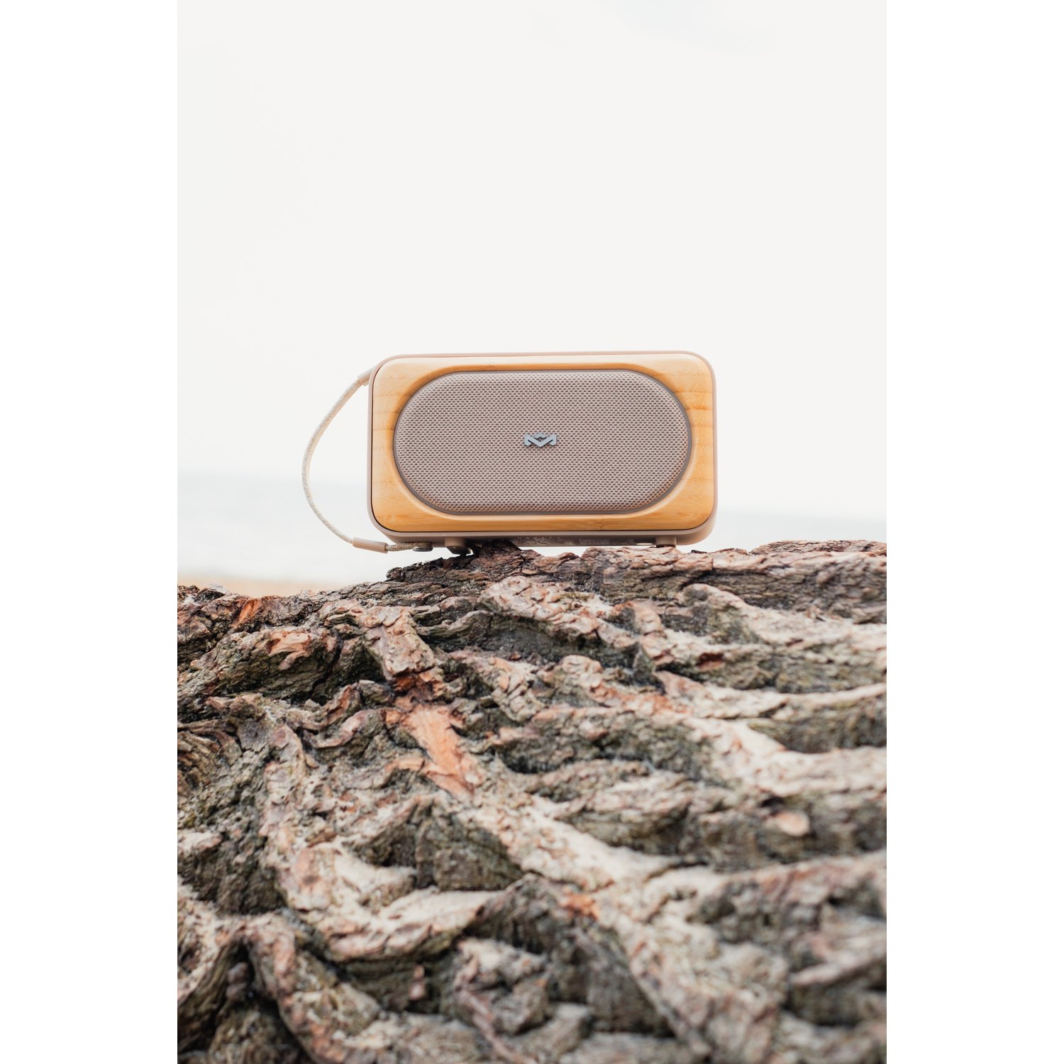 Houten luidspreker op een boomstam, met een beige luidsprekercover en een riem.