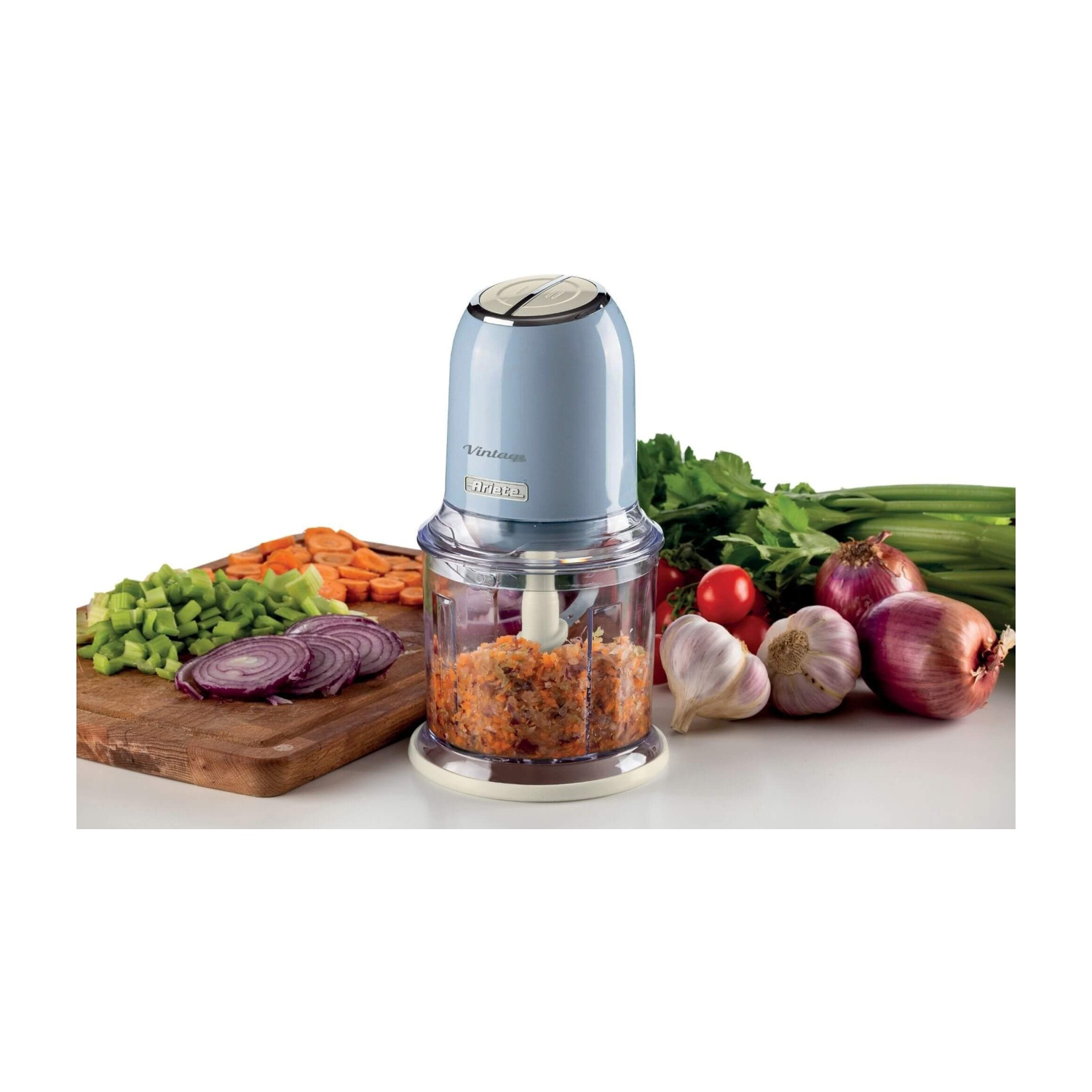 Un tritatutto elettrico blu con verdure e ingredienti tritati su un tagliere di legno vicino.