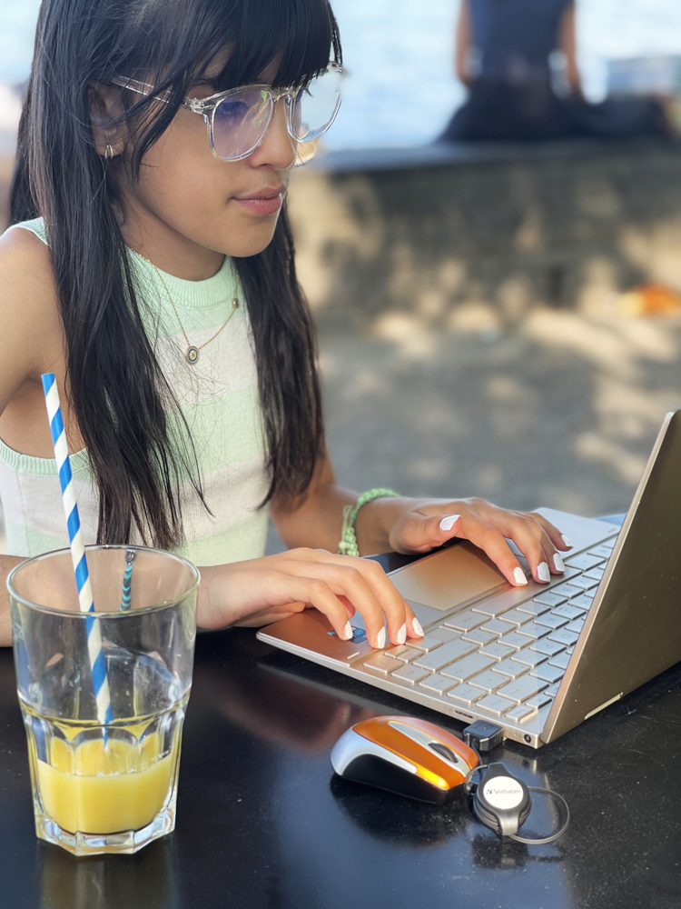 Dziewczyna pracująca na laptopie, z napojem i myszką obok.