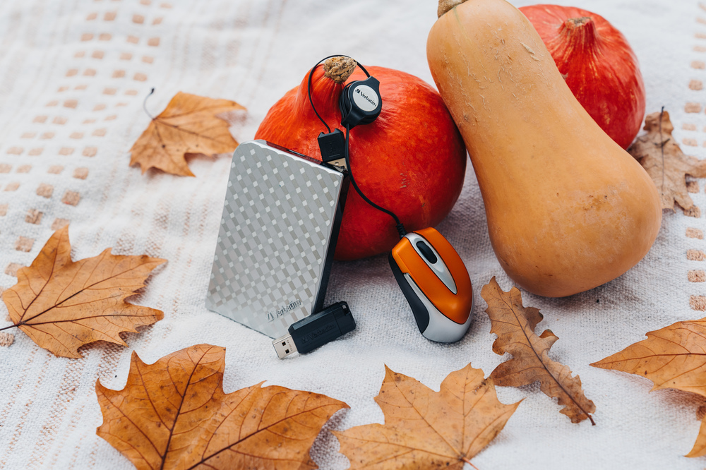 Jesienna sceneria z dyniami, liśćmi, myszą i przenośnym dyskiem twardym.