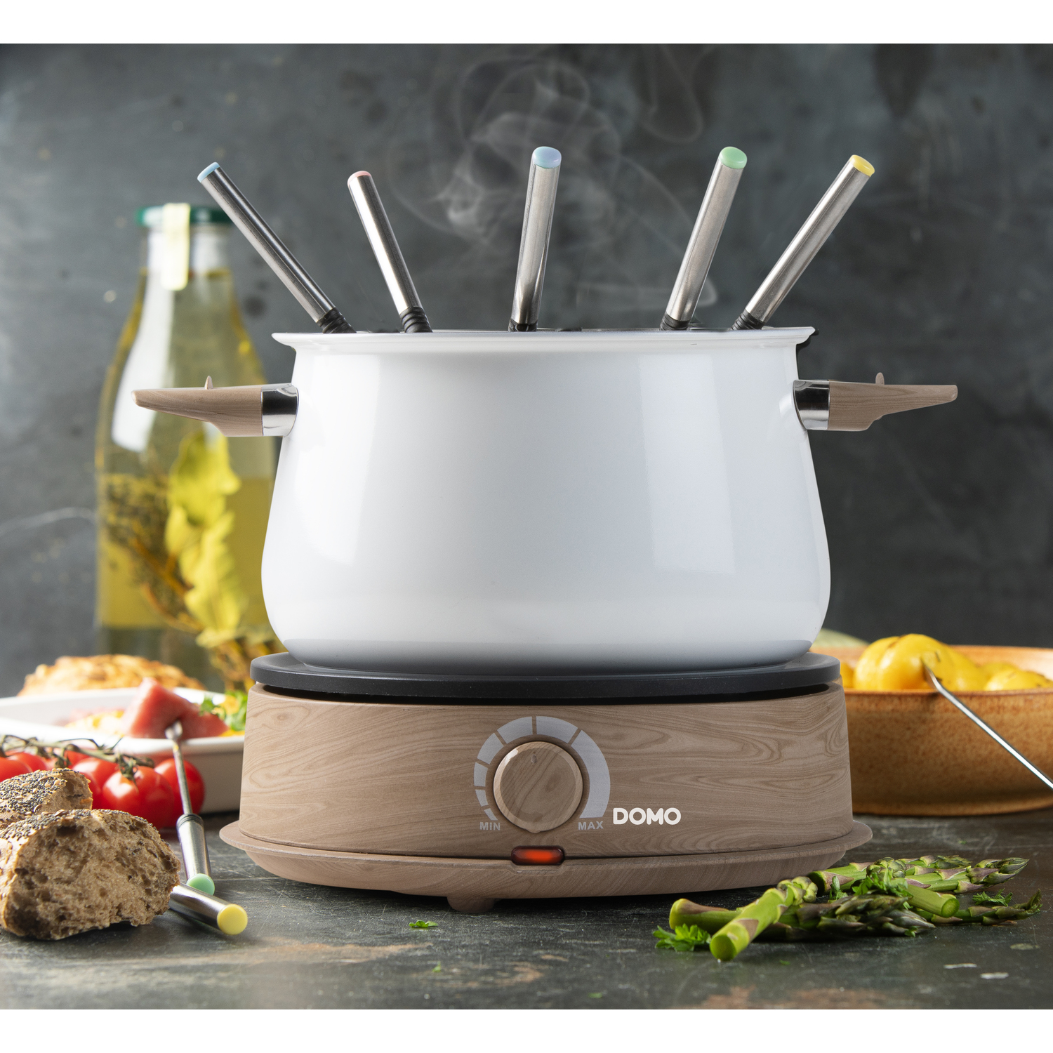 A fondue pot on a wooden base with food and spoons.