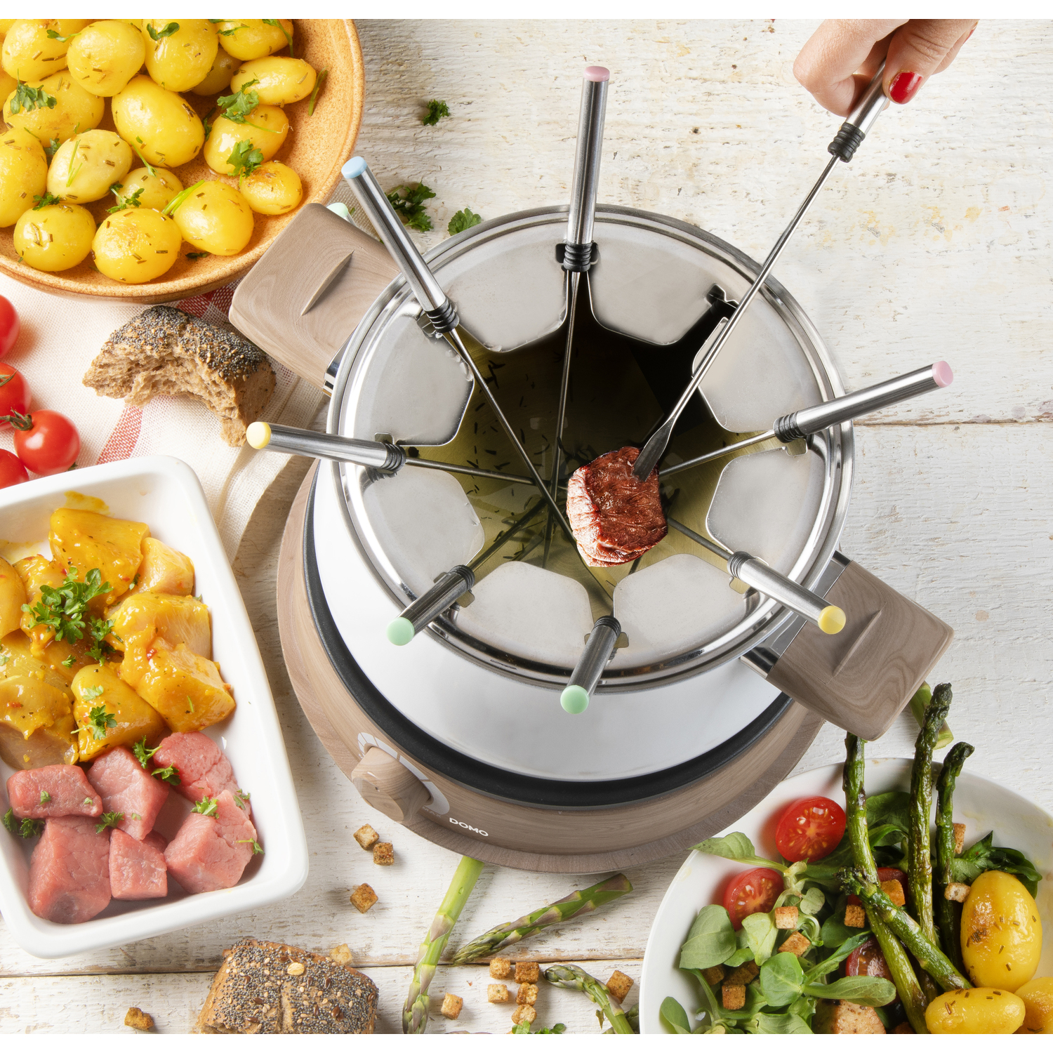 A fondue set with various foods, including meat, vegetables, and bread, arranged on a wooden table.