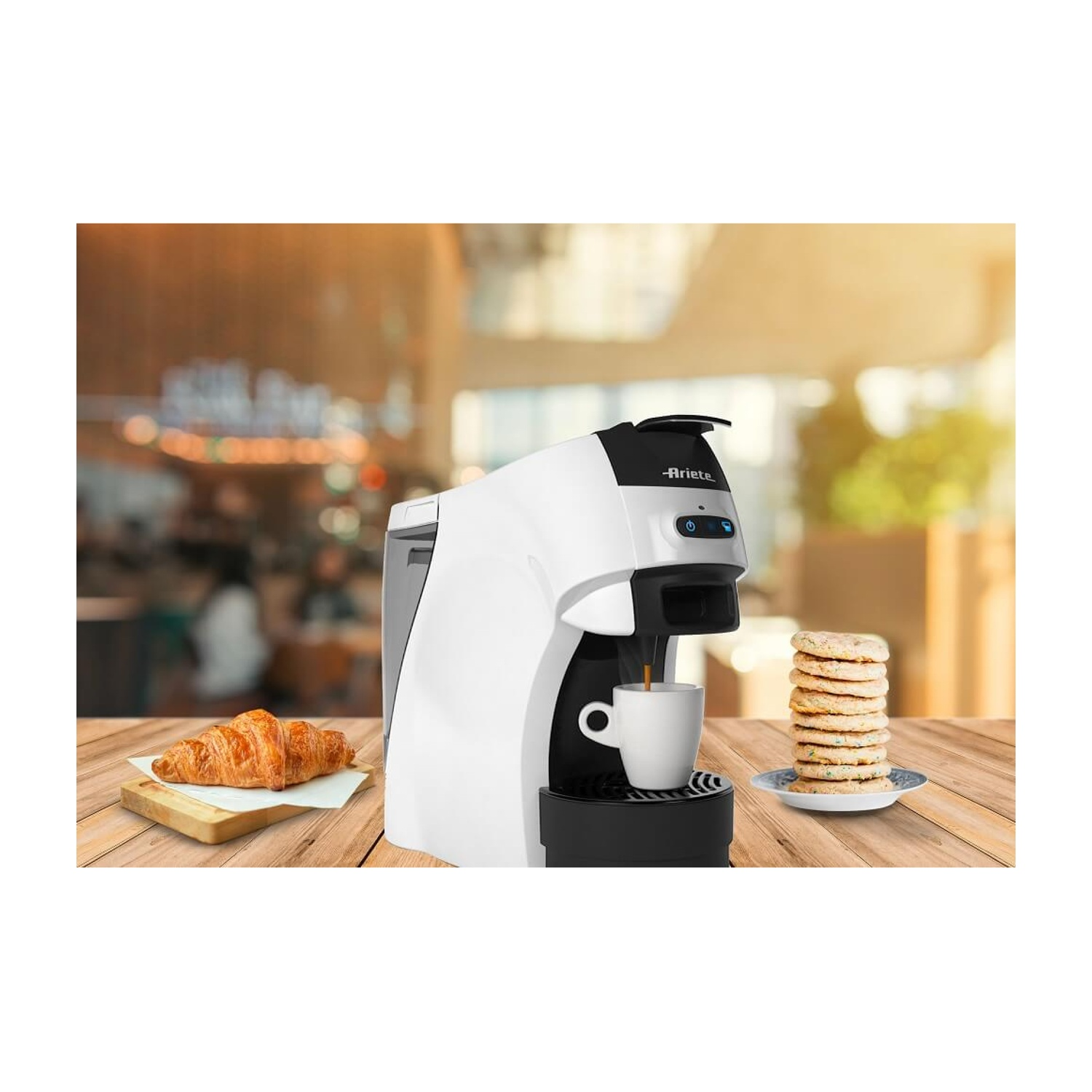 Macchina da caffè bianca con tazza, croissant e biscotti sul tavolo.