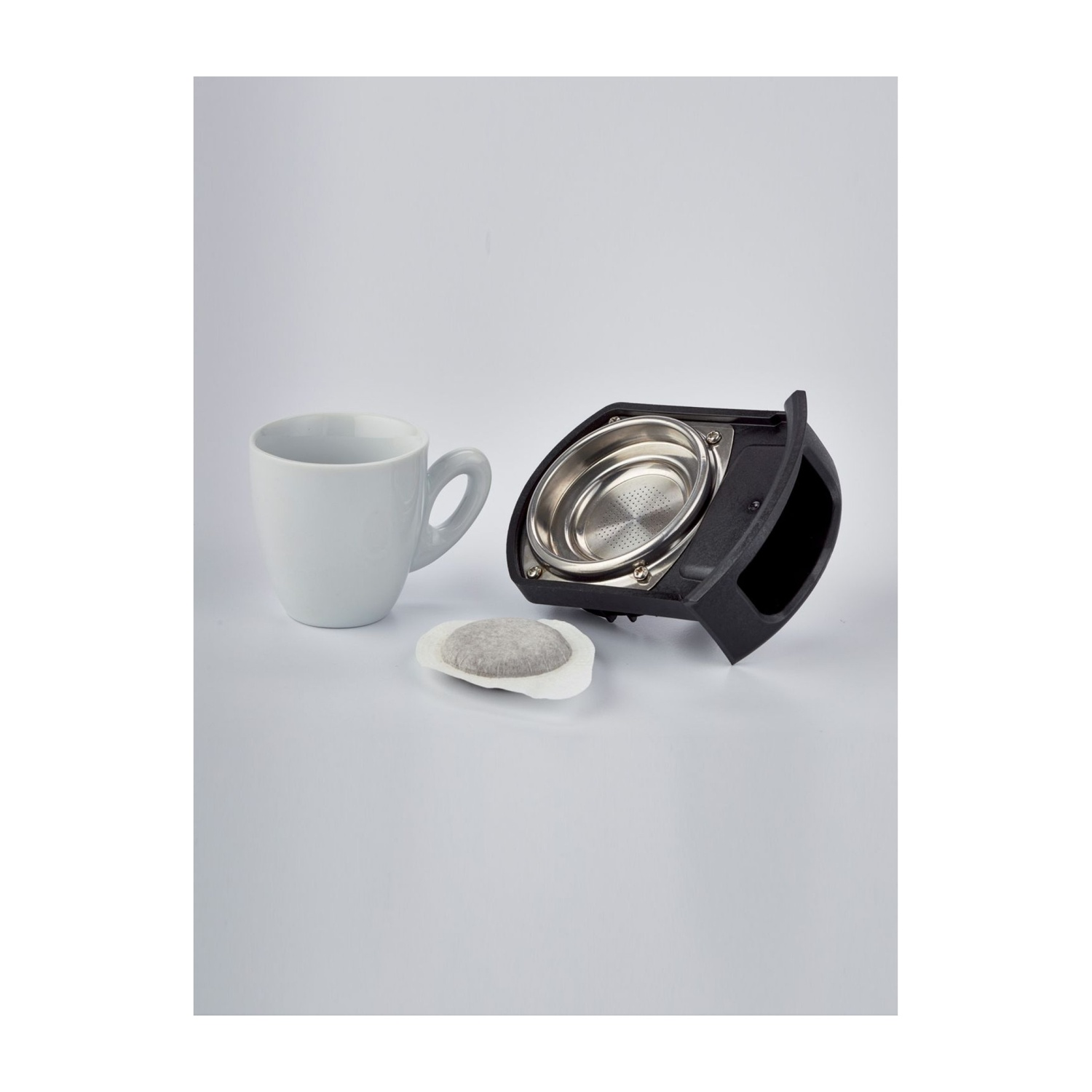 Tazza bianca, parte smontata di macchina del caffè e cialda su superficie bianca.