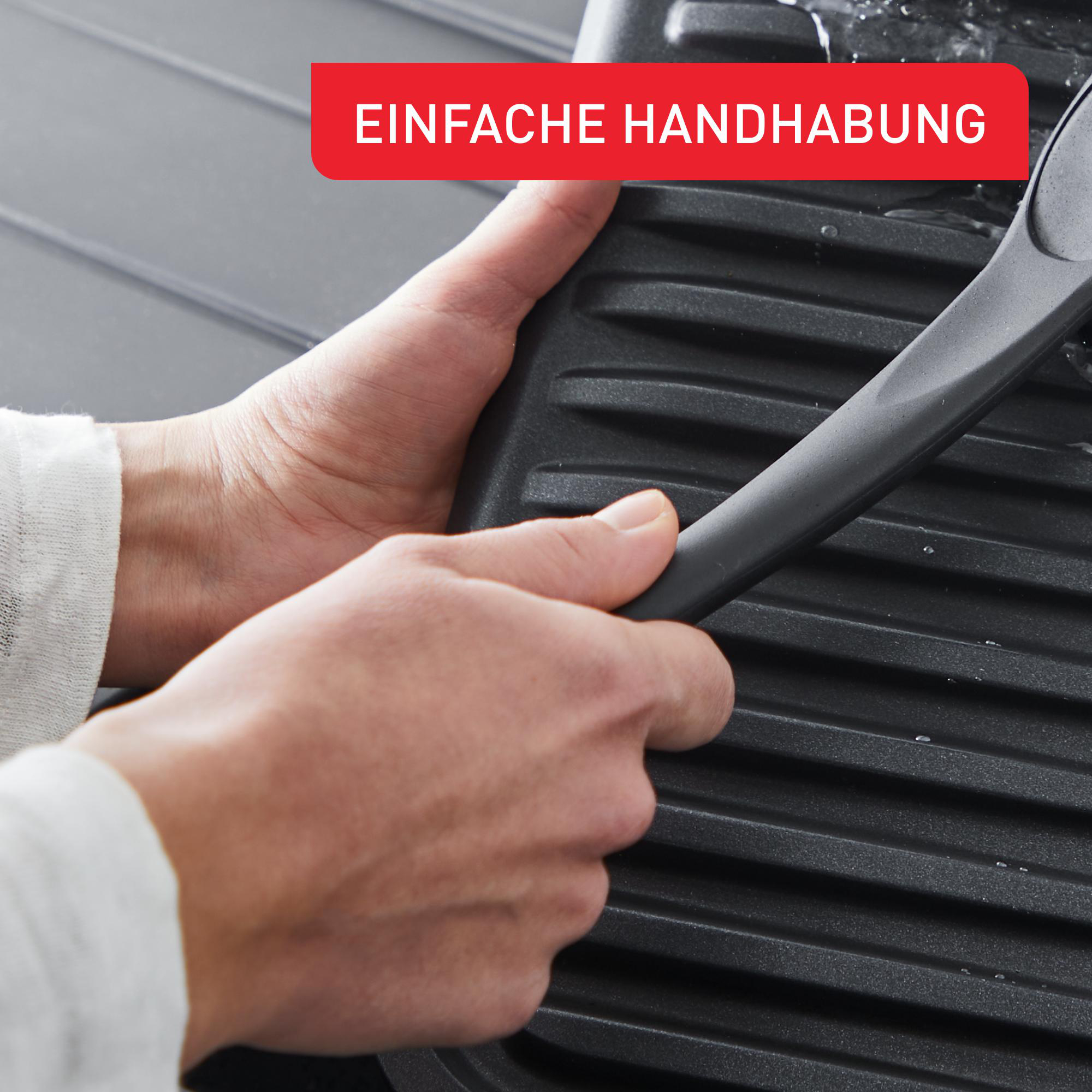 Hände reinigen einen schwarzen Grill mit einer Bürste.