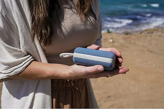 Kobieta trzymająca niebiesko-biały głośnik. Głośnik trzymany jest oburącz.