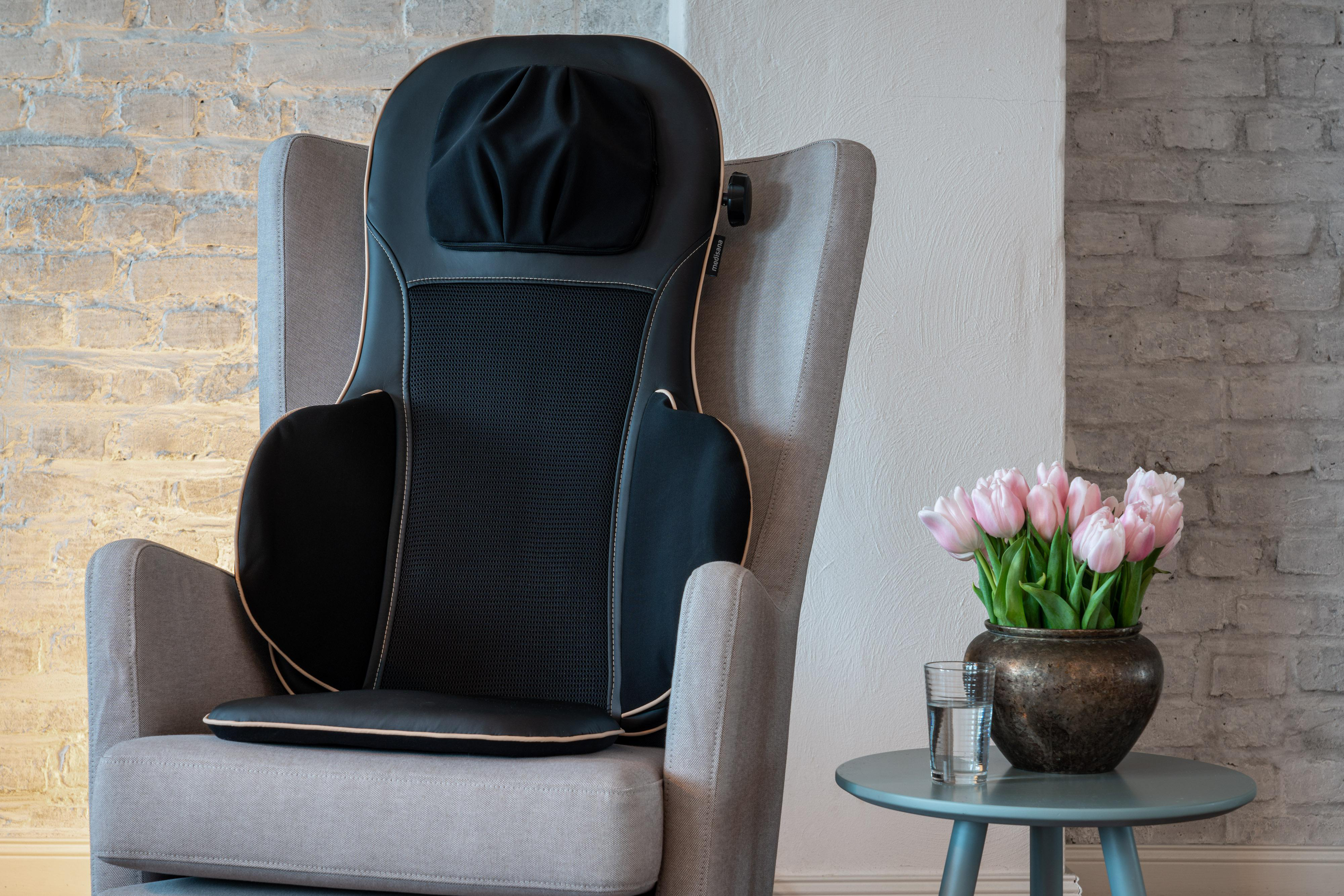 Sessel mit Massagekissen und einer Vase mit rosa Tulpen.