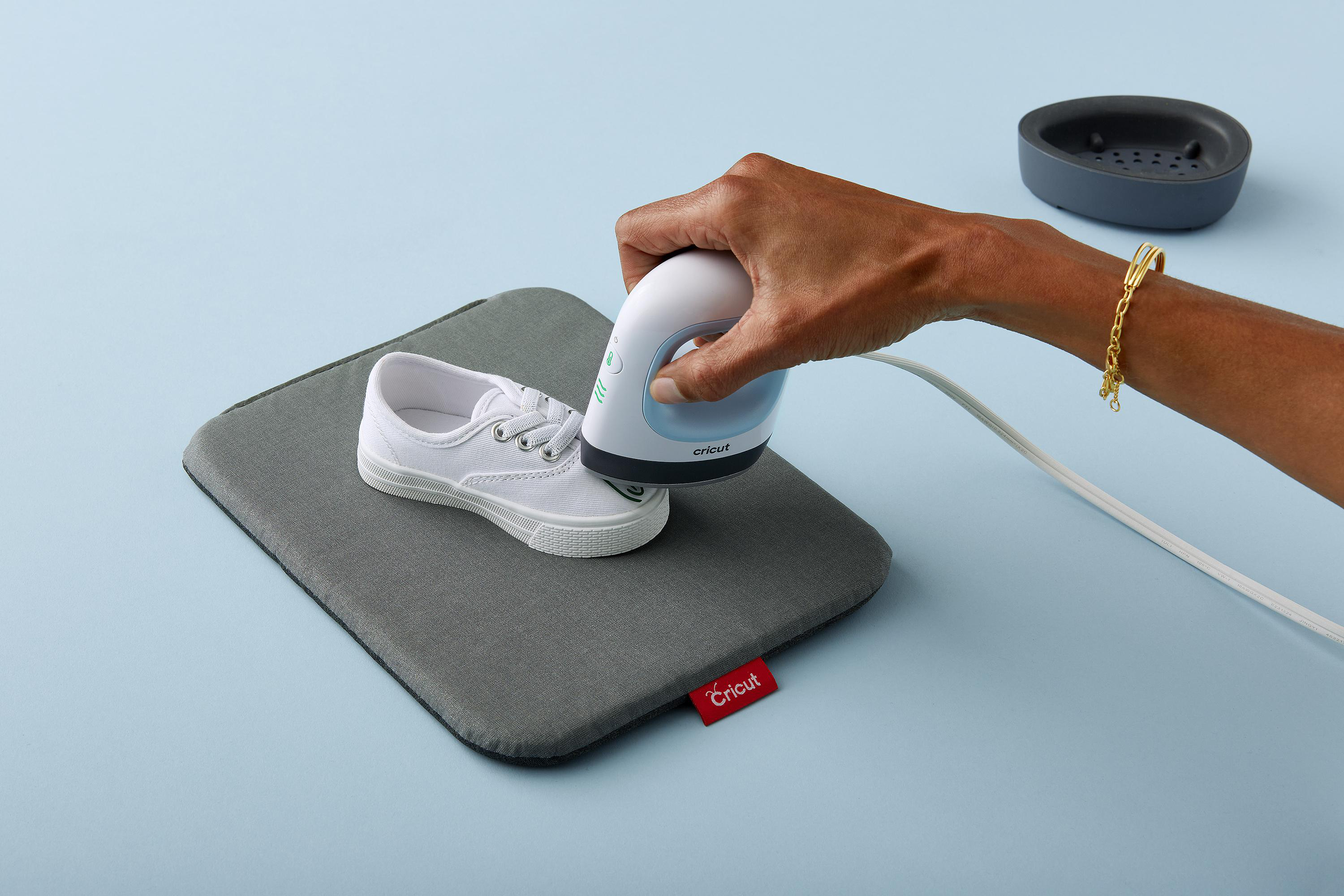 Eine Hand bügelt einen kleinen weißen Schuh auf einem grauen Pad, mit blauem Hintergrund.
