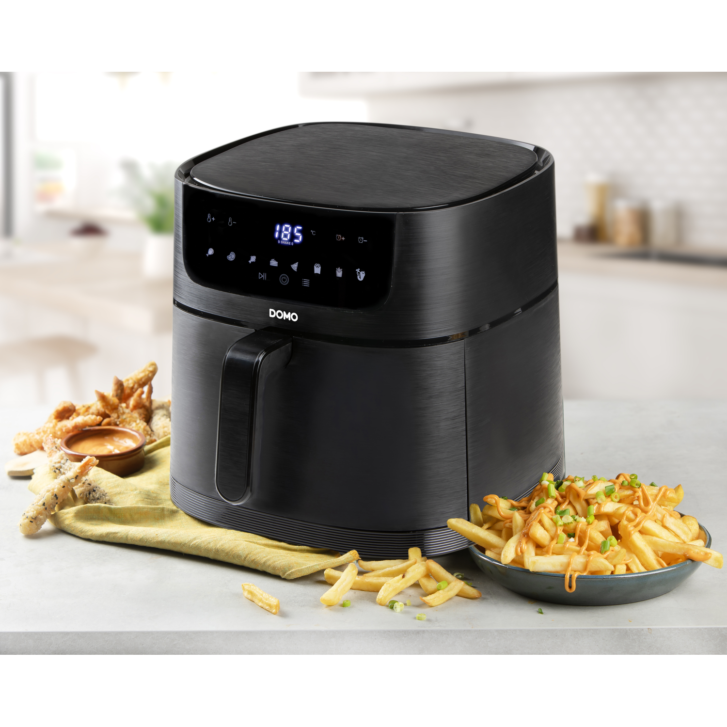 Black air fryer with fries and a sauce bowl on a table.