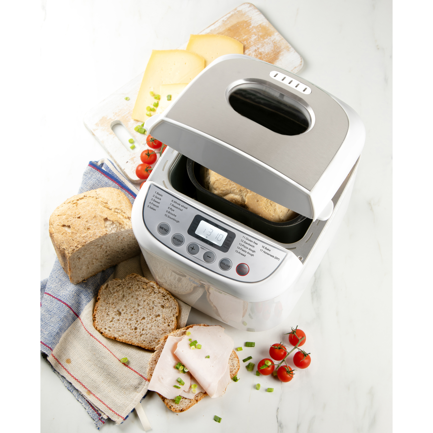 Broodmachine met brood, kaas, sneetjes brood met vlees en lente-uitjes, tomaten en een brood op een marmeren oppervlak.