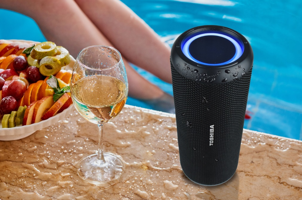 Czarny głośnik Toshiba stoi na mokrej powierzchni w pobliżu kieliszka wina i patery z owocami.