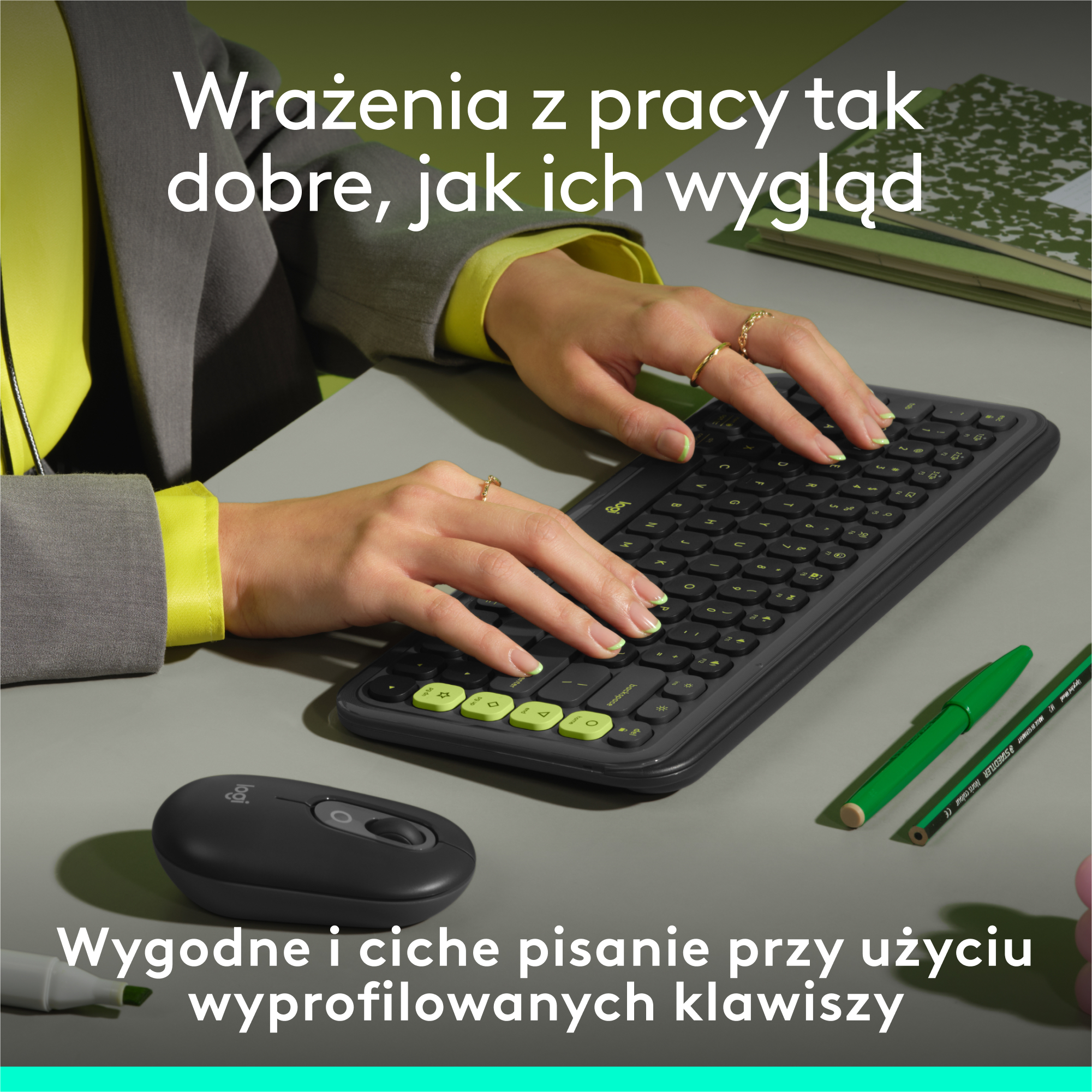 Dłonie kobiety piszą na czarnej klawiaturze z myszą i notatnikiem. Na biurku są też zielone ołówki.