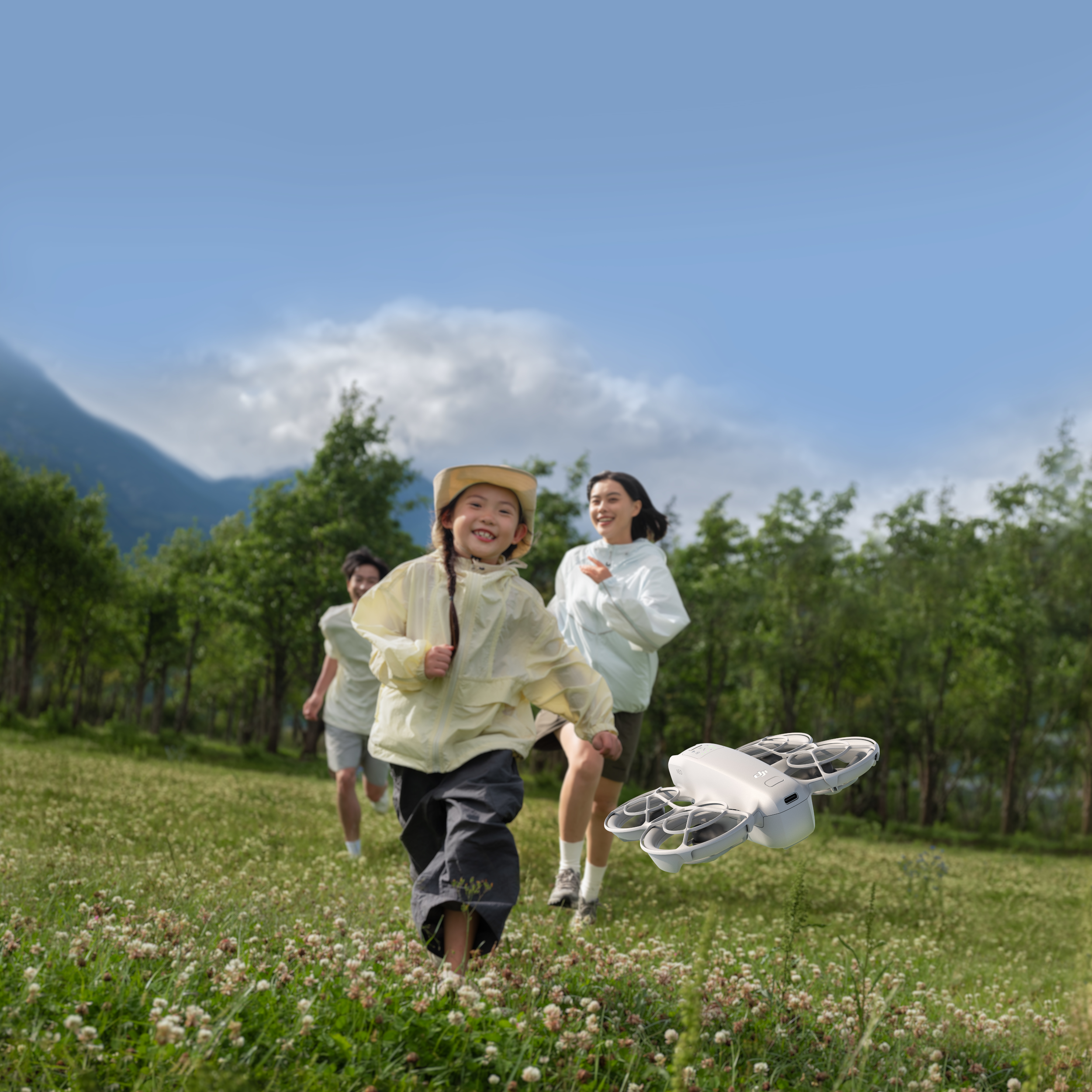Des enfants et un adulte poursuivant un drone dans un champ vert par une journée ensoleillée.