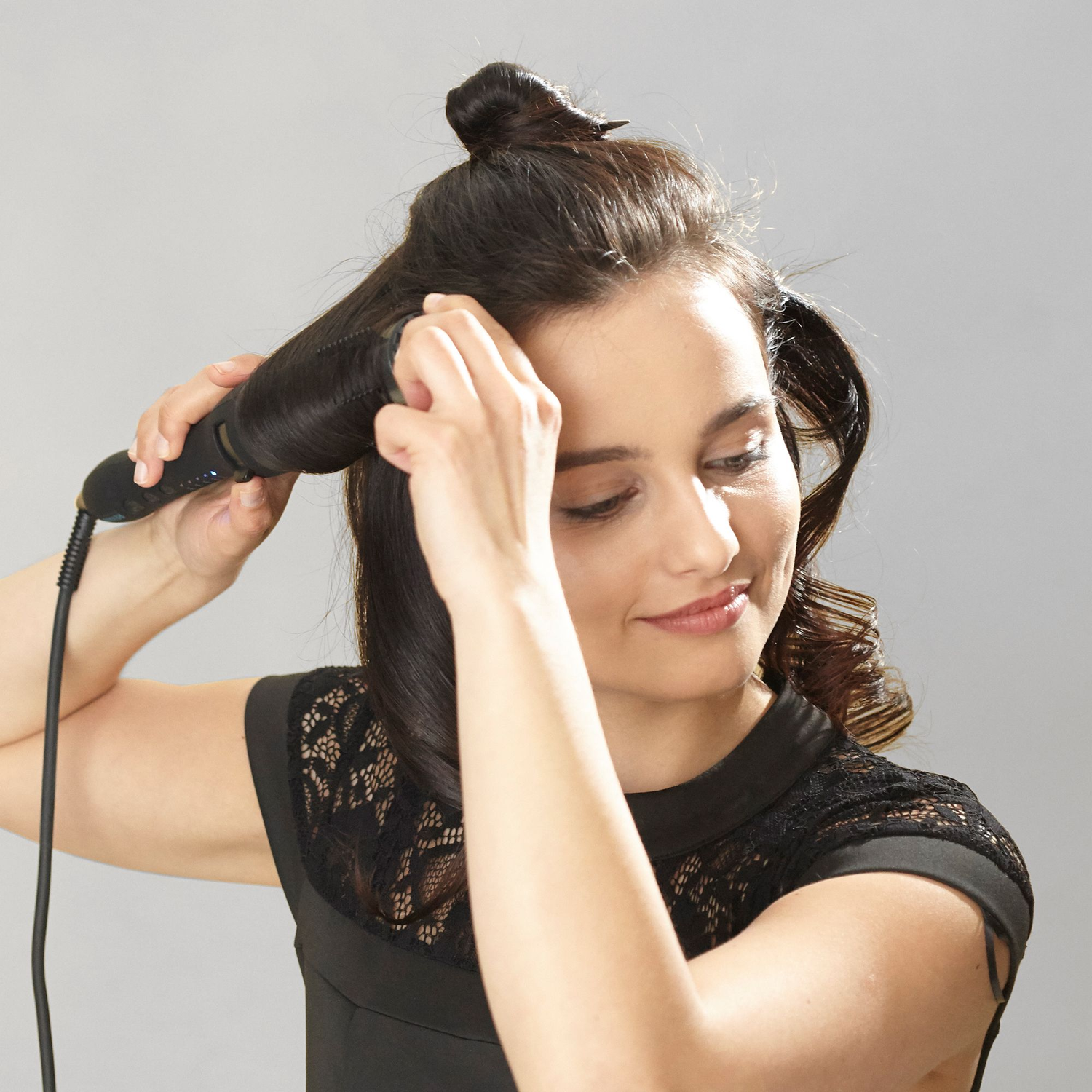 Woman curling her hair with a curling iron. She is smiling and looking down.